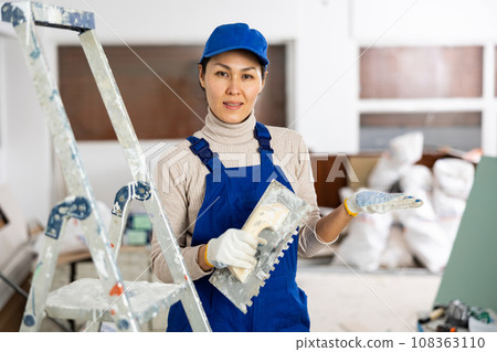 Smiling female repairer with float trowel standing indoors 108363110