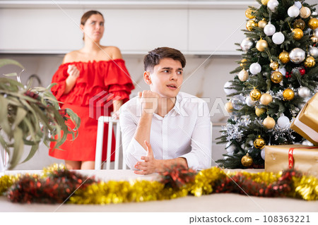 Furious young European man and woman in red dress yelling at each other during preparations for New Year in cuisine Furious young European man and woman in red dress yelling at each other during preparations for New Year in cuisine 108363221