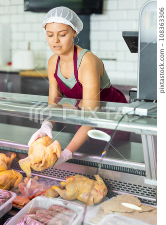 In butcher shop, young female salesperson in gloves shows damp dressed chicken In butcher shop, young female salesperson in gloves shows damp dressed chicken 108363306