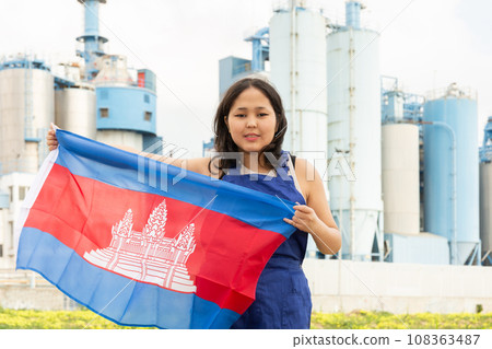 Happy asian girl in work clothes with flag of cambodia standing in front of industrial scenery 108363487