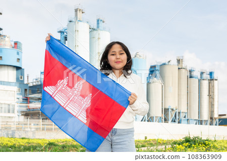 Happy young woman with flag of Cambodia against background of factory Happy young woman with flag of Cambodia against background of factory 108363909