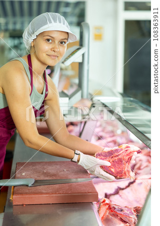 Positive young saleswoman demonstrating piece of meat in butcher shop 108363911