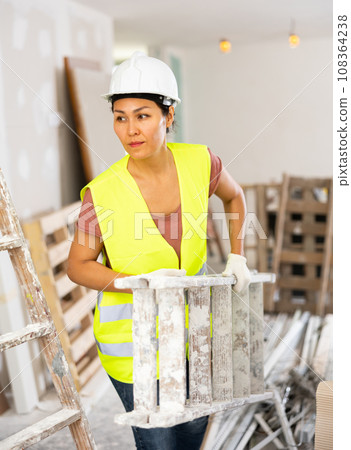Woman repairer carrying stepladder, working in construction site 108364238