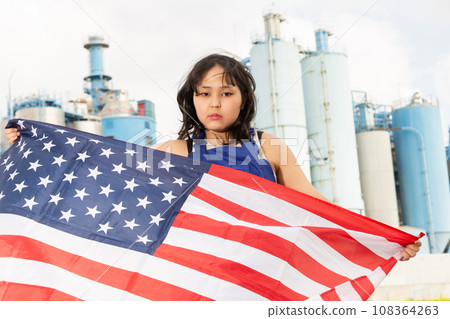 Sad young woman with flag of the USA against background of factory Sad young woman with flag of the USA against background of factory 108364263