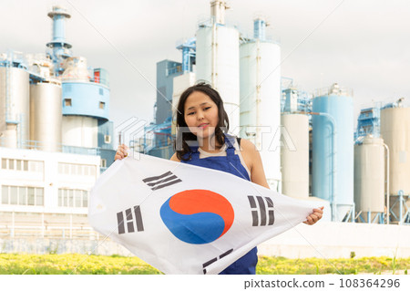 Happy young woman with flag of South Korea against background of factory 108364296