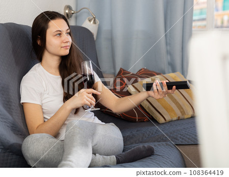 Woman drinking wine watching TV at home Woman drinking wine watching TV at home 108364419
