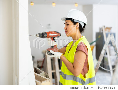 Asian woman construction worker drilling hole in wall Asian woman construction worker drilling hole in wall 108364453