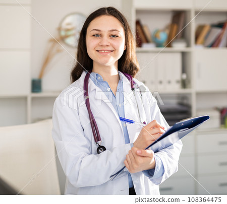 Doctor trainee who is undergoing an internship at the clinic makes important notes on a tablet while standing in a office Doctor trainee who is undergoing an internship at the clinic makes important notes on a tablet while standing in a office 108364475