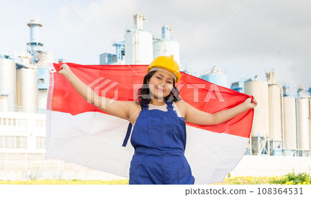 National flag of Indonesia in the hands of girl in overalls against background of modern metallurgical plant 108364531