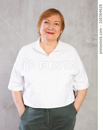 Smiling elderly woman in white shirt with hands in pockets Smiling elderly woman in white shirt with hands in pockets 108364626
