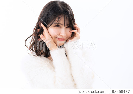 A middle-aged woman wearing a knitwear doing skin care against a white background A middle-aged woman wearing a knitwear doing skin care against a white background 108368427