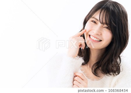 A middle-aged woman wearing a knitwear doing skin care against a white background A middle-aged woman wearing a knitwear doing skin care against a white background 108368434