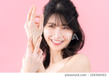 A middle-aged woman doing skin care with a pink background 108368483