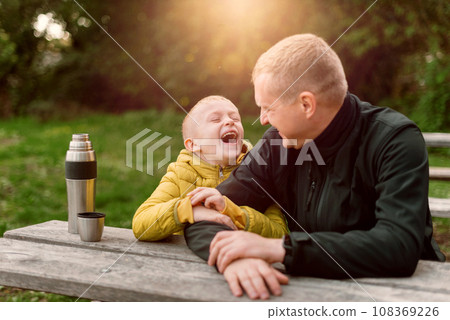 Happy Family: Father And Child Boy Son Playing And Laughing In Autumn Park, Sitting On Wooden Bench And Table. Father And Little Kid Having Fun Outdoors, Playing Together. Father And Son Sitting On A 108369226