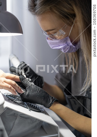 Manicurist at work. Professional manicurist removes old worn nail design from nails of client using modern electric drill. Preparing fingernails for making fresh manicure and applying new nail design 108369708