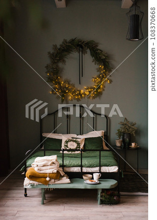 Christmas interior of a cozy bedroom with a bed and a wreath on the wall Christmas interior of a cozy bedroom with a bed and a wreath on the wall 108370668