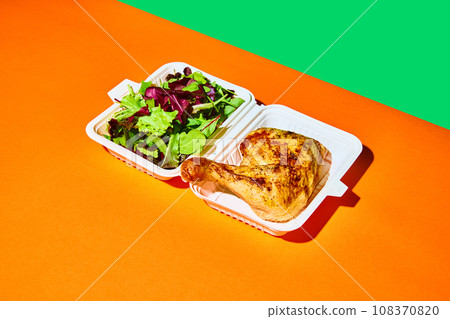 Top view. Close up image of opened paper box with salad and baked chicken against orange-green background. Concept of fast food, delivery. 108370820