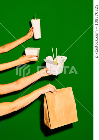 Take it away. Close up image of female hands holds paper box and bag and one opened box with noodles against green background. Concept of fast food, delivery. 108370825