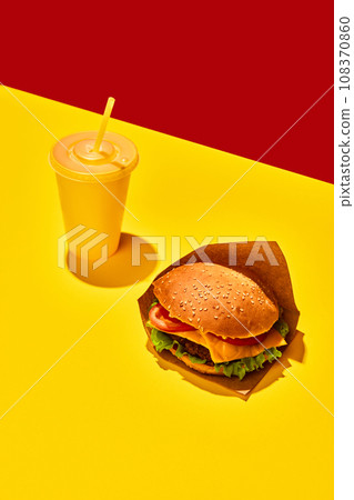 Tasty hamburger with beef sauces and vegetables with refreshing drinks against vivid red-yellow background. Concept of fast food, delivery. 108370860