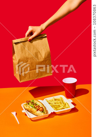 Tasty hotdog with sausage served mustard and ketchup with green salad with refreshing drinks and fried potato against vivid red background. Concept of fast food, delivery. Tasty hotdog with sausage served mustard and ketchup with green salad with refreshing drinks and fried potato against vivid red background. Concept of fast food, delivery. 108370863