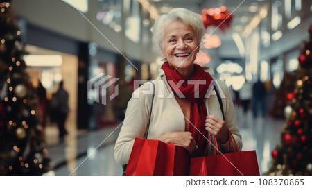 Smiling middle-aged woman with Christmas gifts in shopping bags in a shopping mall. Christmas sale 108370865