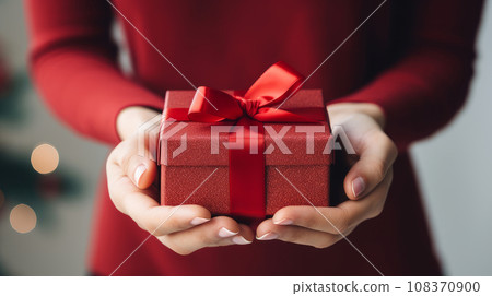 Christmas gift in a red box in gentle female hands New Year's background with bokeh and copy space Christmas gift in a red box in gentle female hands New Year's background with bokeh and copy space 108370900