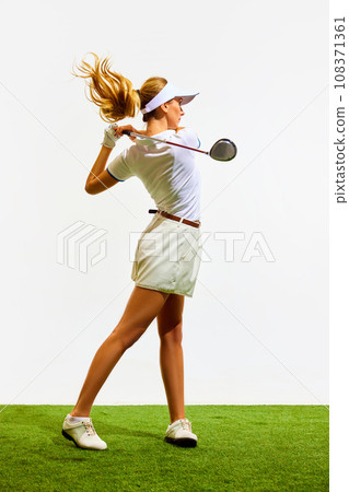 Beautiful, sportive, blonde, young girl with slim, fit body playing golf on grass, teeing off isolated over white background 108371361