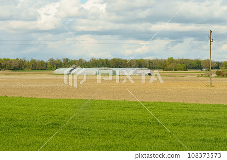 Greenhouses for growing vegetables located behind a plowed field in the spring. Greenhouses for growing vegetables located behind a plowed field in the spring. 108373573