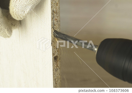 Furniture assembly. A worker drills a hole in a piece of cabinet furniture. Furniture assembly. A worker drills a hole in a piece of cabinet furniture. 108373606