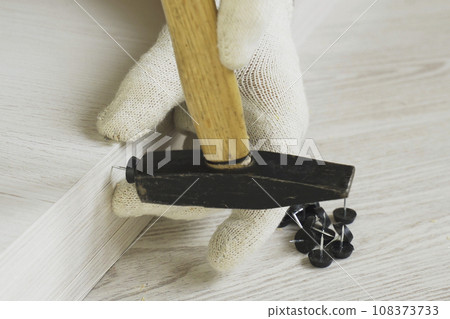 A worker hammers a furniture support - a nail - to a piece of cabinet furniture. A worker hammers a furniture support - a nail - to a piece of cabinet furniture. 108373733