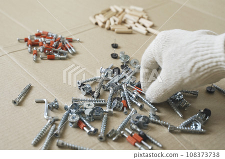 A male worker goes through the furniture fasteners after unpacking, preparing to assemble the furniture. A male worker goes through the furniture fasteners after unpacking, preparing to assemble the furniture. 108373738