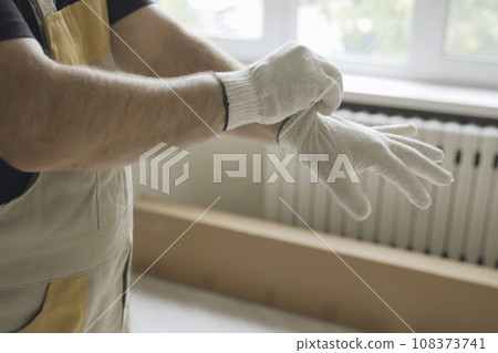 The worker stands in the room and puts on gloves before starting work. 108373741