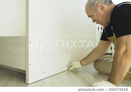 A worker fastens the parts of a bed using confirmat. A worker fastens the parts of a bed using confirmat. 108373838