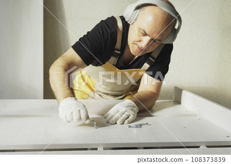 A worker fastens the parts of a bed using a confirmat. A worker fastens the parts of a bed using a confirmat. 108373839