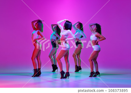Beautiful, elegant, attractive women dancing high heel dance over pink studio background in neon light Beautiful, elegant, attractive women dancing high heel dance over pink studio background in neon light 108373895