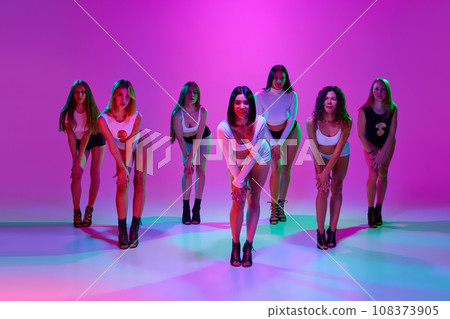 Group of beautiful women dance high heel dance, training over pink studio background in neon light 108373905