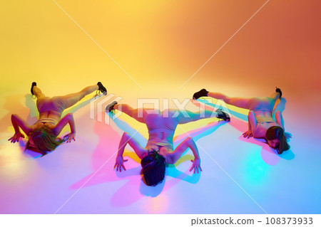 Freedom of movements. Three young woman in underwear dancing high heel dance on floor over gradient yellow background in neon light Freedom of movements. Three young woman in underwear dancing high heel dance on floor over gradient yellow background in neon light 108373933