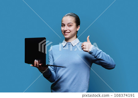 Serious teenage student girl using laptop on blue background, showing finger up Serious teenage student girl using laptop on blue background, showing finger up 108374191