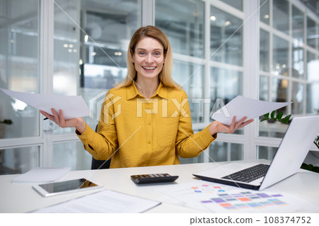 Portrait happy successful woman financier doing paperwork, businesswoman holding papers, documents, contracts and reports in hand, smiling joyfully, satisfied working with laptop, using calculator 108374752