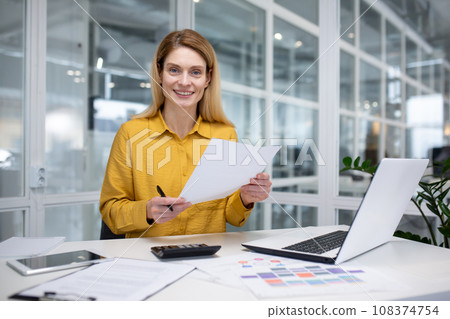 Portrait happy successful woman financier doing paperwork, businesswoman holding papers, documents, contracts and reports in hand, smiling joyfully, satisfied working with laptop, using calculator 108374754