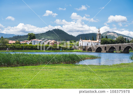 Bridge across the river in Ponte de Lima, southern bank, medieval bridge dates back to 1368, view of the church, river back, mountains or hills on the background, selective focus Bridge across the river in Ponte de Lima, southern bank, medieval bridge dates back to 1368, view of the church, river back, mountains or hills on the background, selective focus 108375978