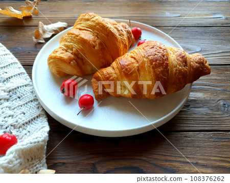 There is a plate with freshly baked croissants on the wooden table. There is a plate with freshly baked croissants on the wooden table. 108376262