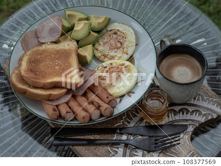 breakfast is including Fried sausages, Fried eggs, Toast breads and cut avocados served with Honey and Cup of coffee. breakfast is including Fried sausages, Fried eggs, Toast breads and cut avocados served with Honey and Cup of coffee. 108377569