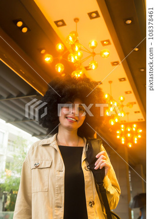 Woman with curly black hair illuminated by yellow lamp light 108378461