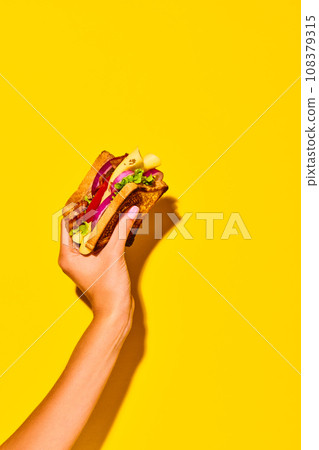 Woman holding delicious sandwich with grilled bread, ham, lettuce, cheese, tomato, onion and avocado over yellow background. Cooking, taste. Poster 108379315