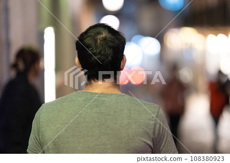 A man walking in a lively street at night - view from behind 108380923
