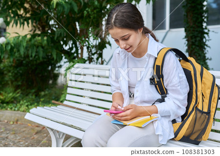 Teenage student girl with backpack using smartphone, texting outdoor Teenage student girl with backpack using smartphone, texting outdoor 108381303