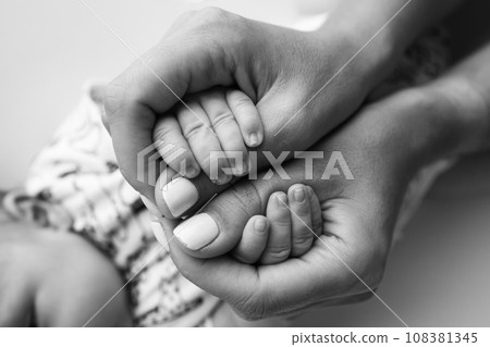 Parents' hands hold the fingers of a newborn baby. The hand of a mother and father close-up holds the fist of a newborn baby. Family health and medical care. Tiny fingers in a black and white photo. Parents' hands hold the fingers of a newborn baby. The hand of a mother and father close-up holds the fist of a newborn baby. Family health and medical care. Tiny fingers in a black and white photo. 108381345