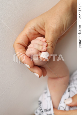 Parents' hands hold the fingers of a newborn baby. The hand of a mother and father close-up holds the fist of a newborn baby. Family health and medical care. Professional photo on white background 108381348