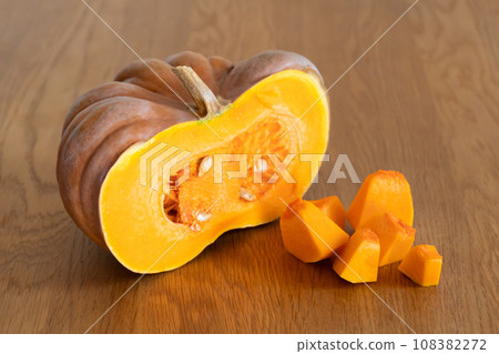 Half of an orange pumpkin next to diced pumpkin pulp on a wooden kitchen table. Half of an orange pumpkin next to diced pumpkin pulp on a wooden kitchen table. 108382272